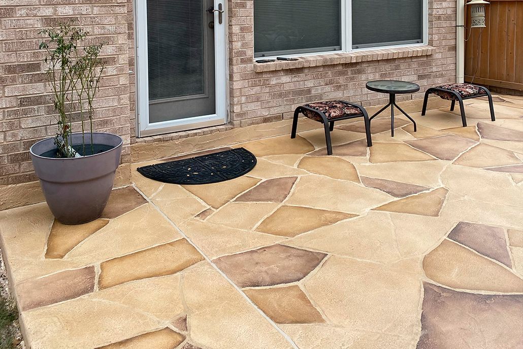 Patio with patterned concrete in tan, brown, and cream with small table, chairs, and potted plant.