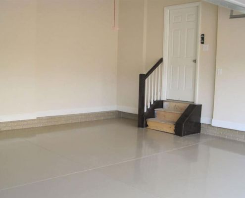 Empty garage with a glossy gray floor and steps leading to a white door.