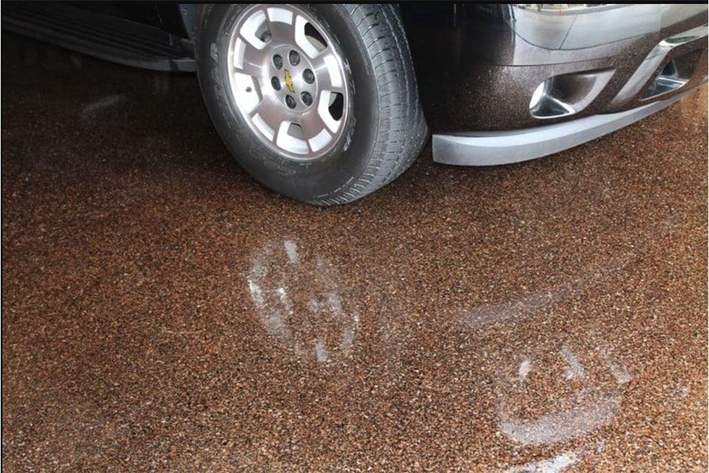 A brown SUV tire and bumper resting on a brown epoxy-coated floor, with visible reflections.