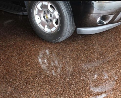 A dark car parked on a textured brown epoxy garage floor with wet tire tracks.