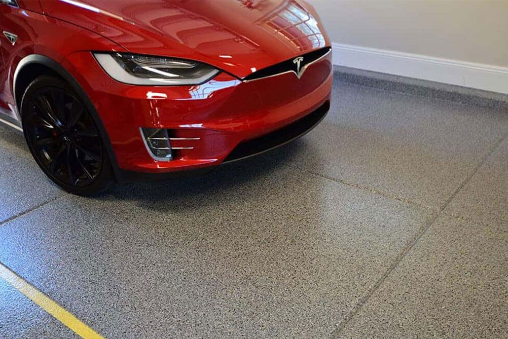 Red Tesla electric car parked on a speckled garage floor, next to a yellow painted line.