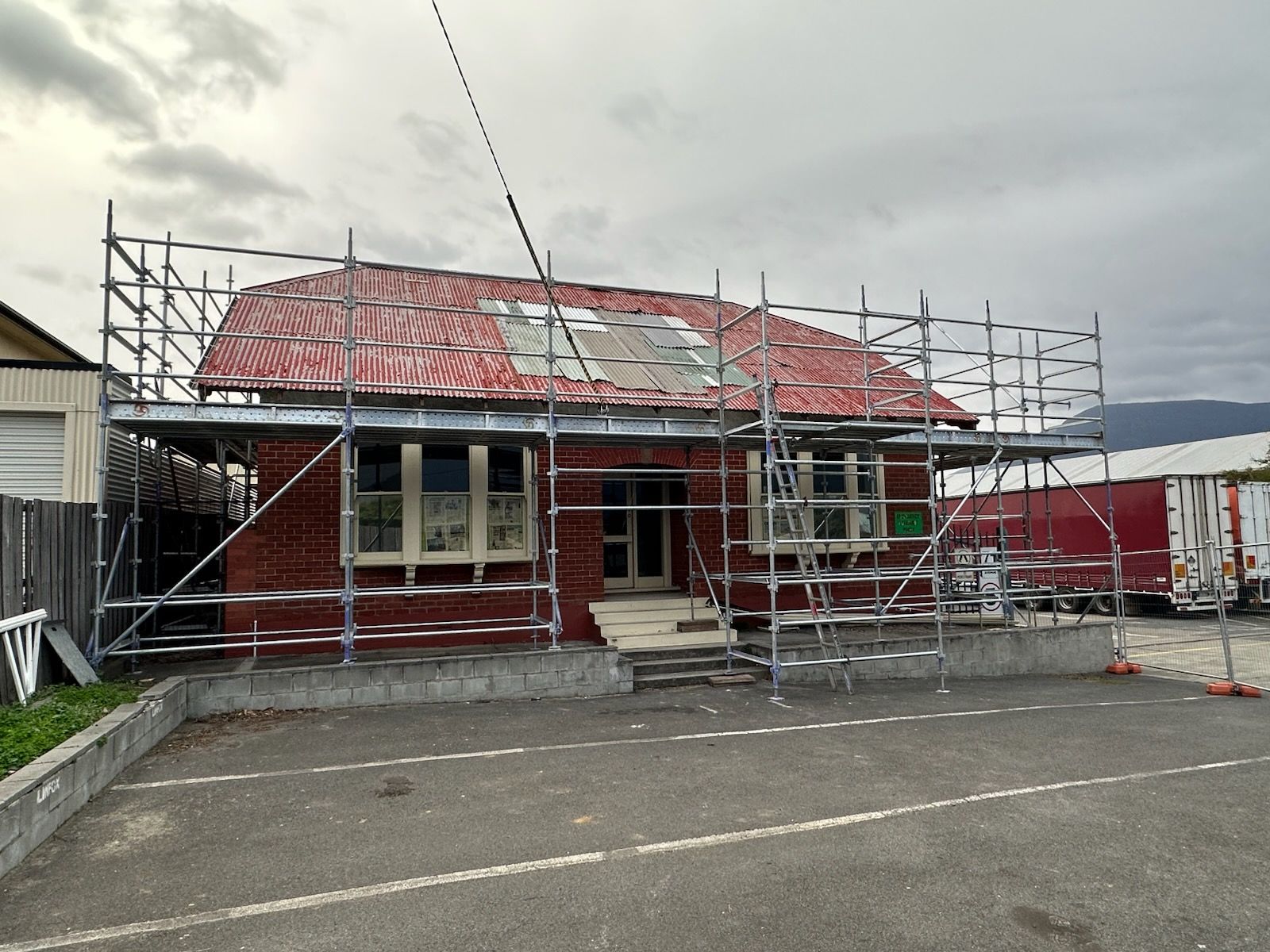 Red house under construction with scaffolding and a partially covered roof by the water