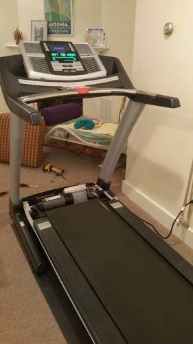A treadmill with open shroud is sitting in a room next to a bed.