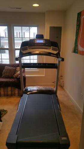 A treadmill is sitting in a living room next to a window.