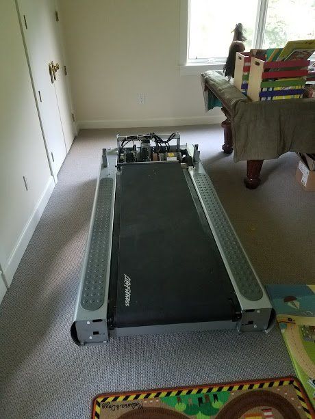 A disassembled treadmill is sitting in a room next to a pool table
