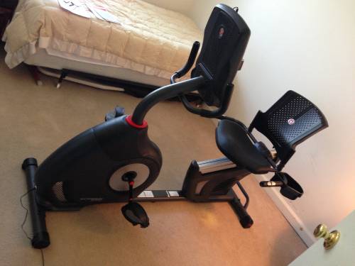 A recumbent exercise bike is in a bedroom next to a bed