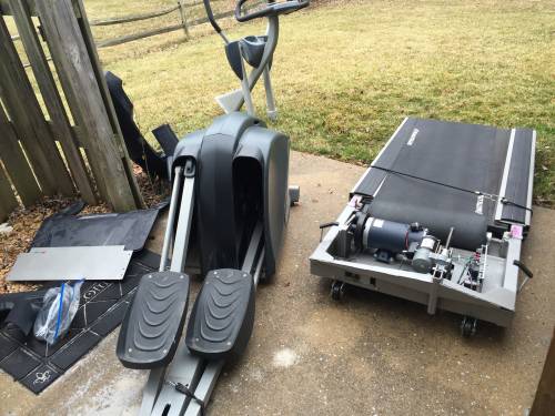 An disassembled elliptical and a treadmill are sitting on a sidewalk.