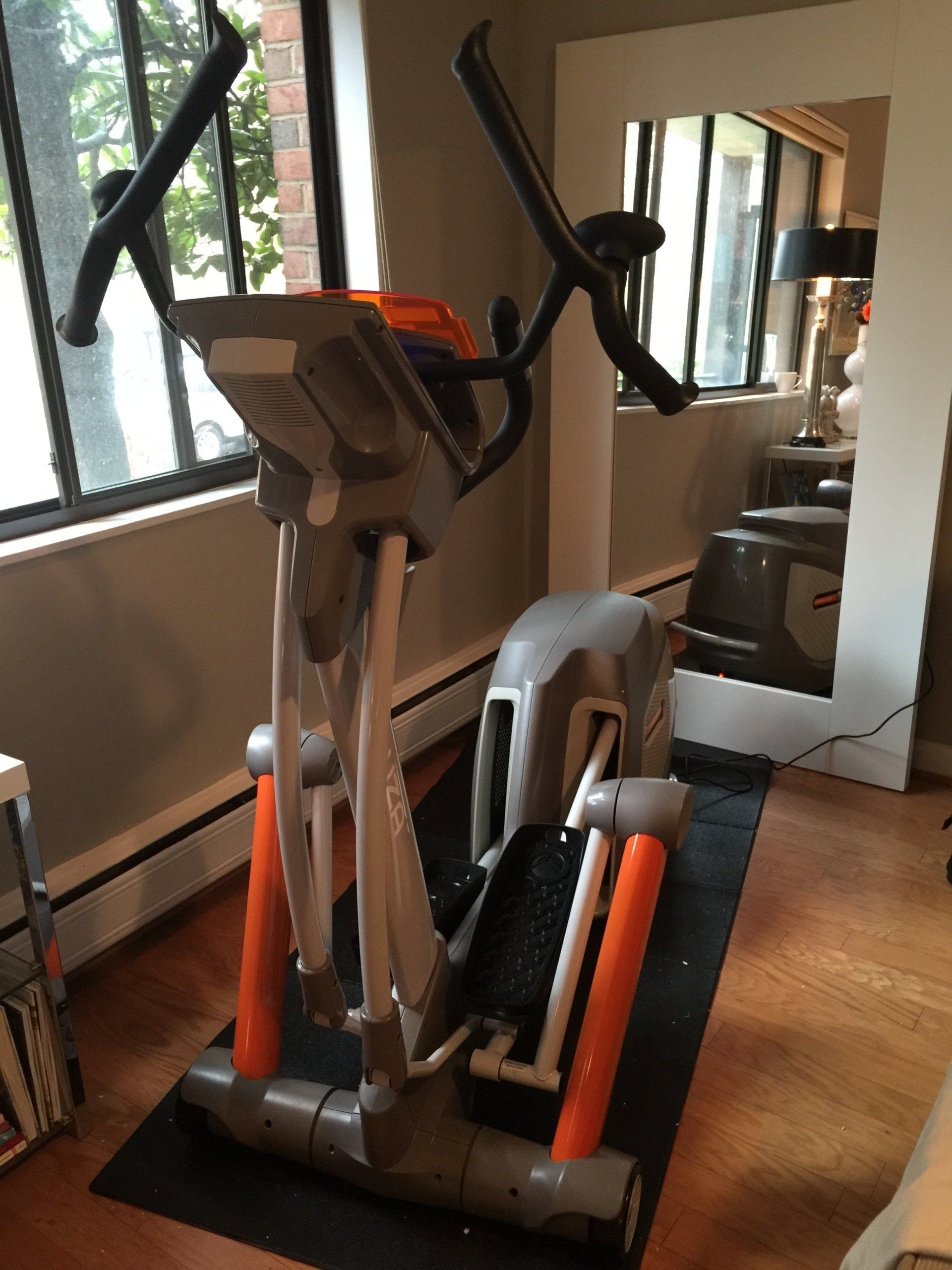 An elliptical is sitting on a mat in front of a mirror