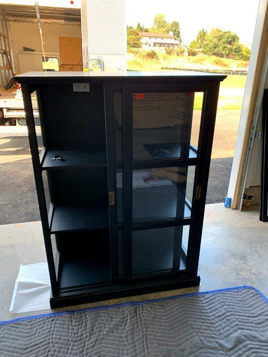 A black cabinet with glass doors is sitting on a blanket in a garage.