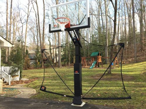 A basketball hoop in a backyard with a playground in the background.