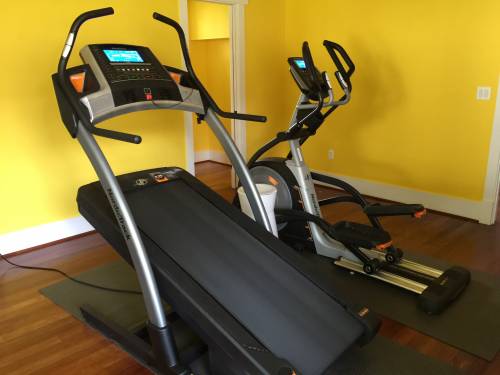 A treadmill and an elliptical are in a room with yellow walls