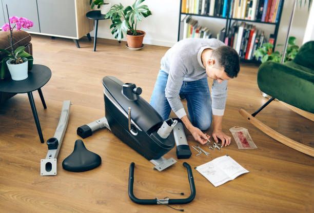 Man assembling stationary bike on hardwood floor.