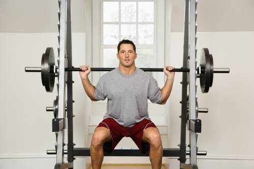 A man is squatting with a barbell in a gym.