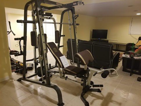 A Marcy home gym in a living room with a bench and a couch.