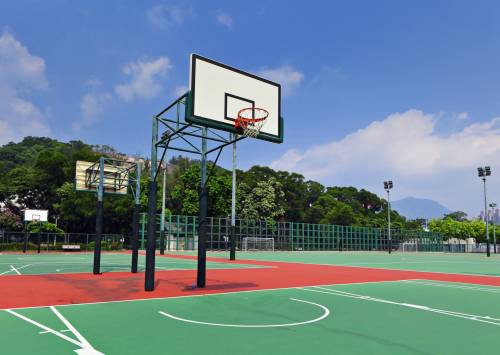 Basketball court with green and red surface, basketball hoops, and a mountainous backdrop.