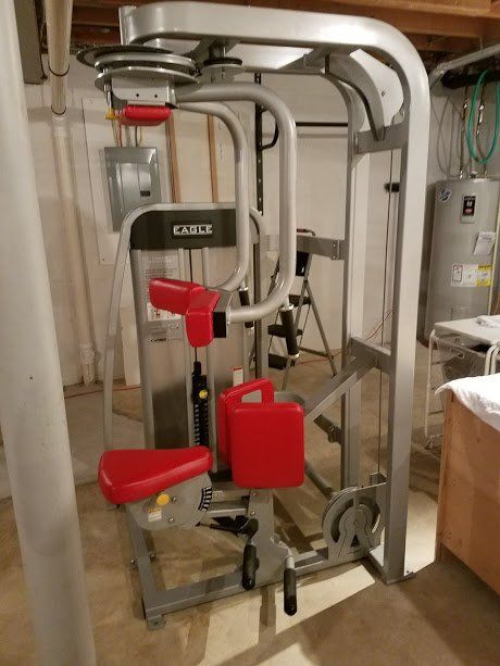 A gym machine with a red seat is sitting in a basement.