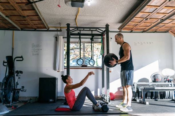 Woman doing sit-ups while a man coaches her in a gym