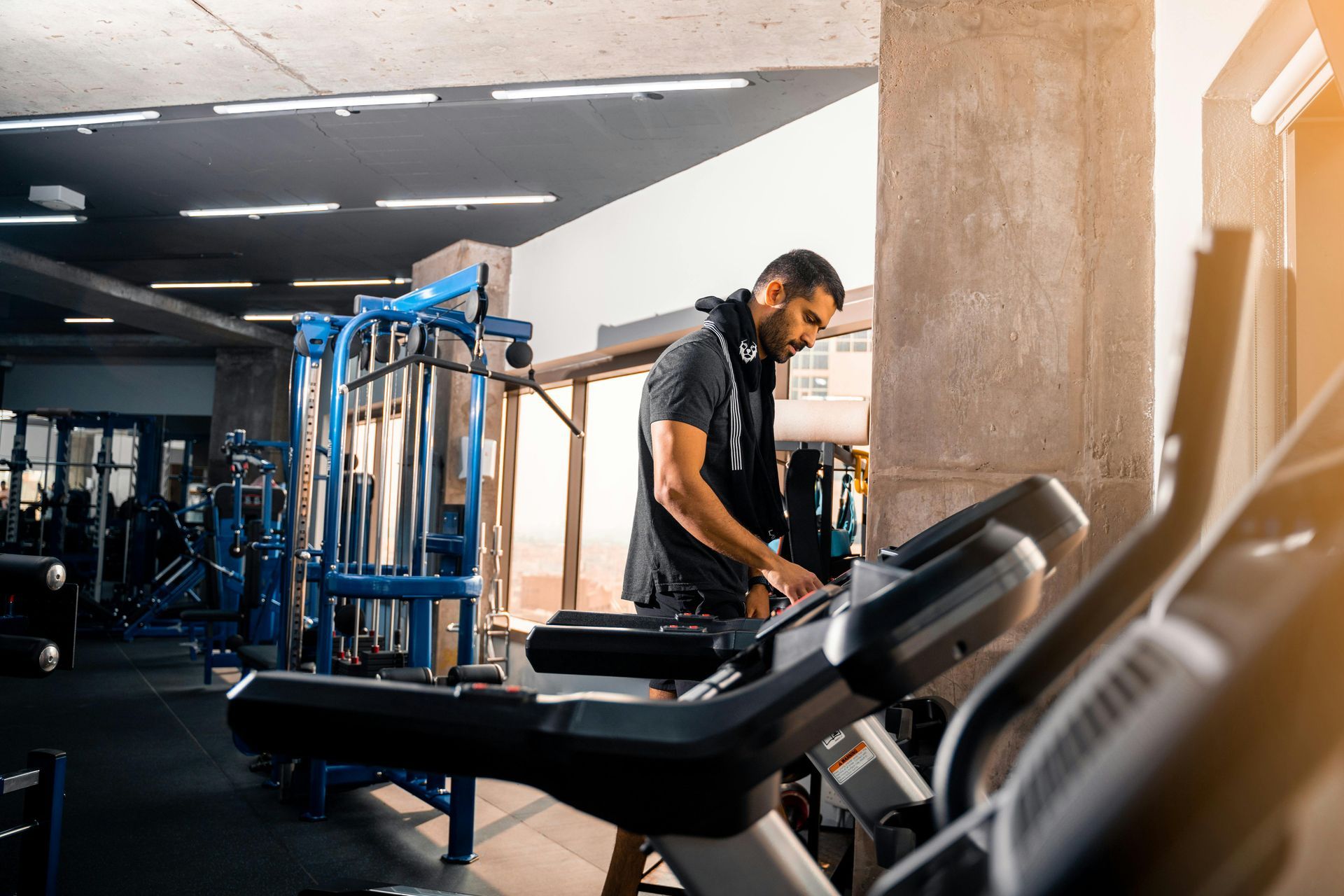 A person in a gym adjusting the settings on a treadmill, with weight machines in the background.