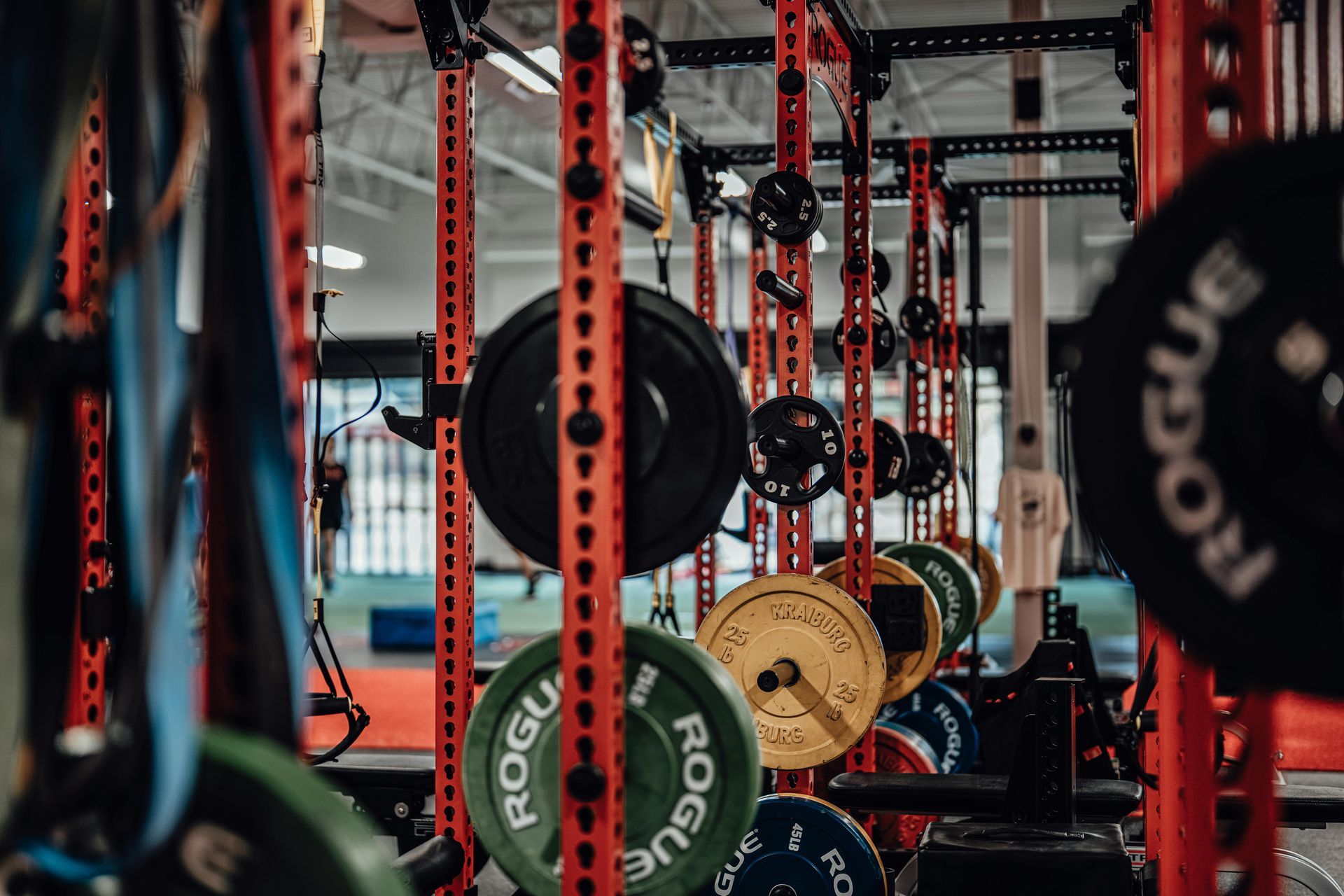Red power racks and weight plates, including Rogue branded discs, in a gym training facility.