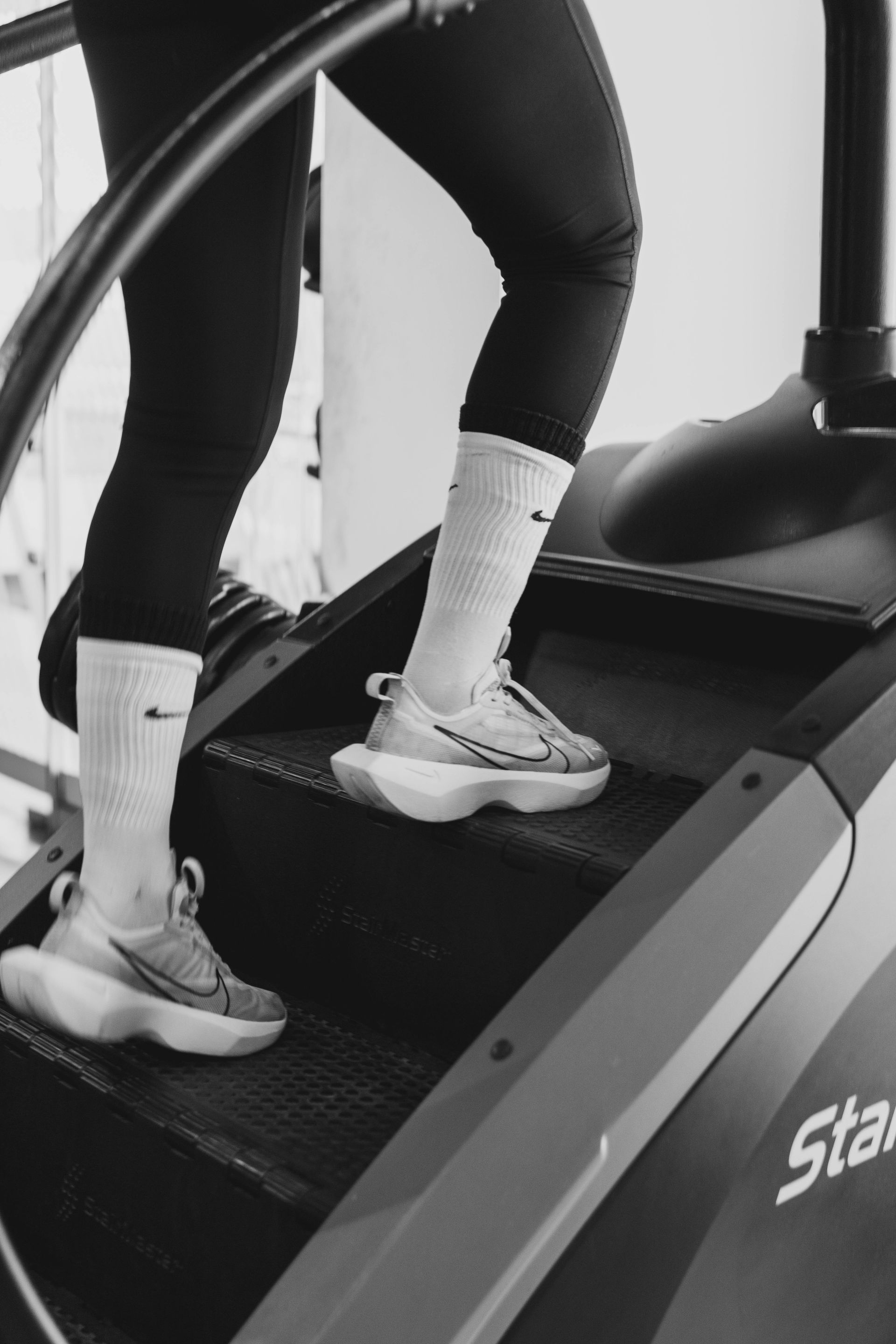 Person walking on a treadmill in a gym, wearing black leggings and white socks with sneakers.
