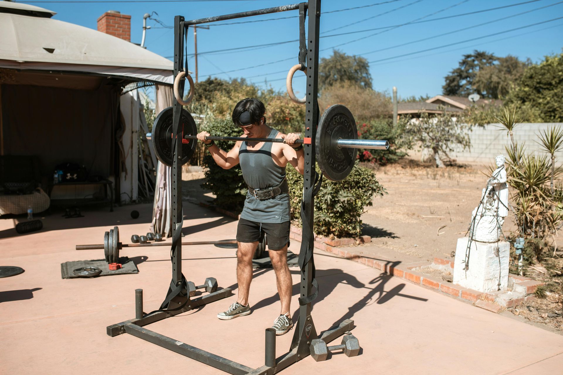 Person lifting a barbell in a backyard home gym setup
