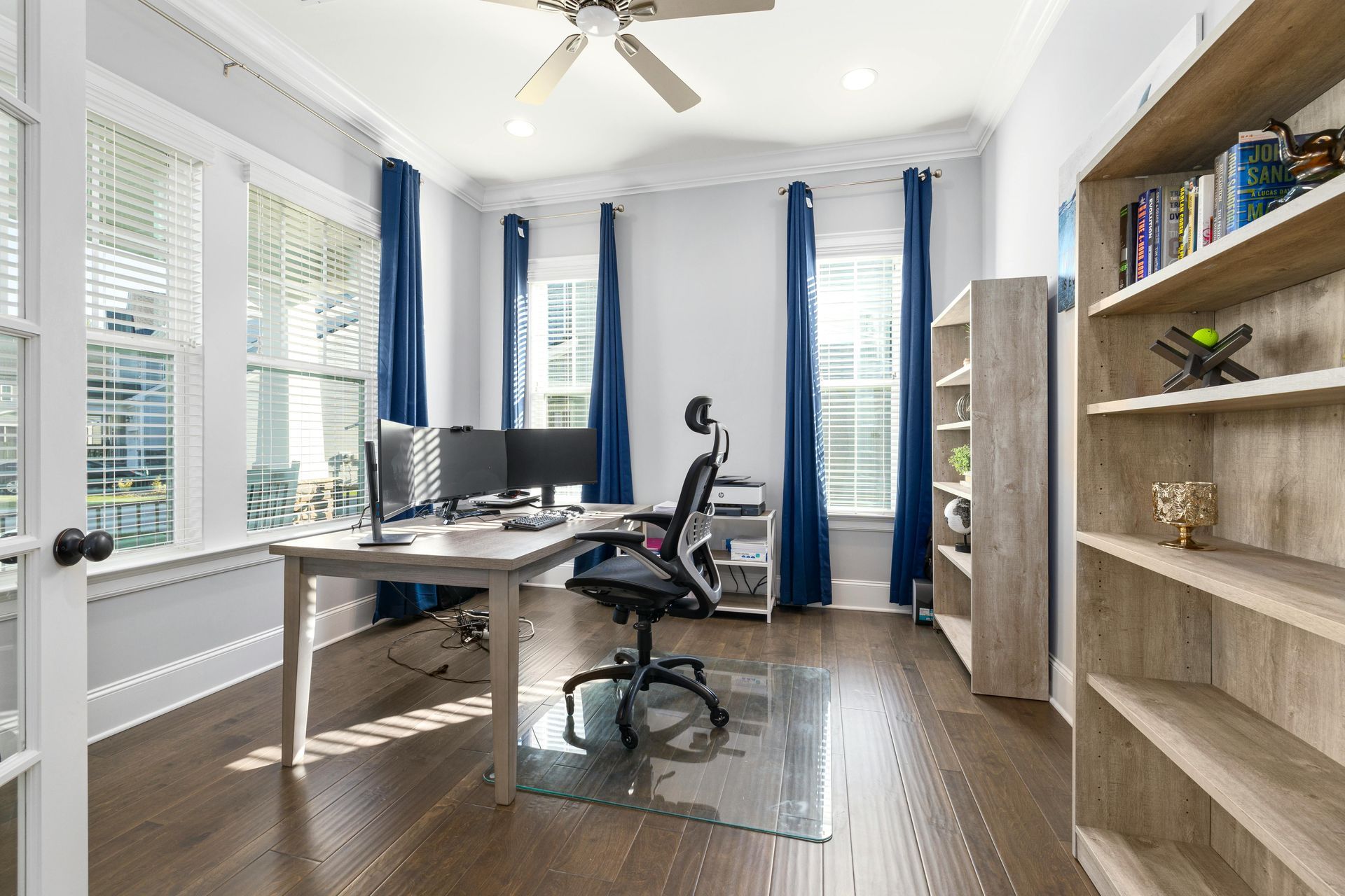 Bright home office with desk, chair, large windows, blue curtains, and bookshelves