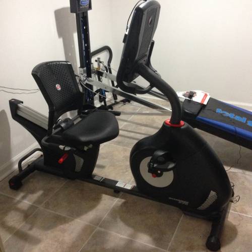 A recumbent exercise bike sits in a room next to a bench
