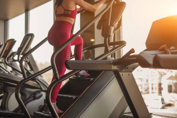 A person in a matching red gym outfit exercises on a stair-climbing machine in a fitness center with windows.