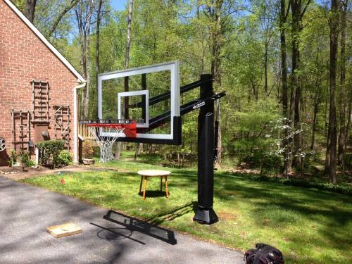 A basketball hoop is sitting in the grass in front of a house.