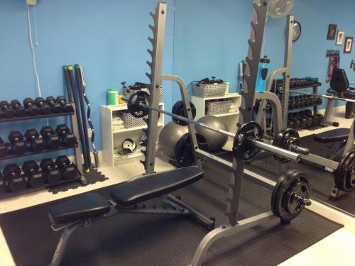 A squat gym with a bench and barbells in it