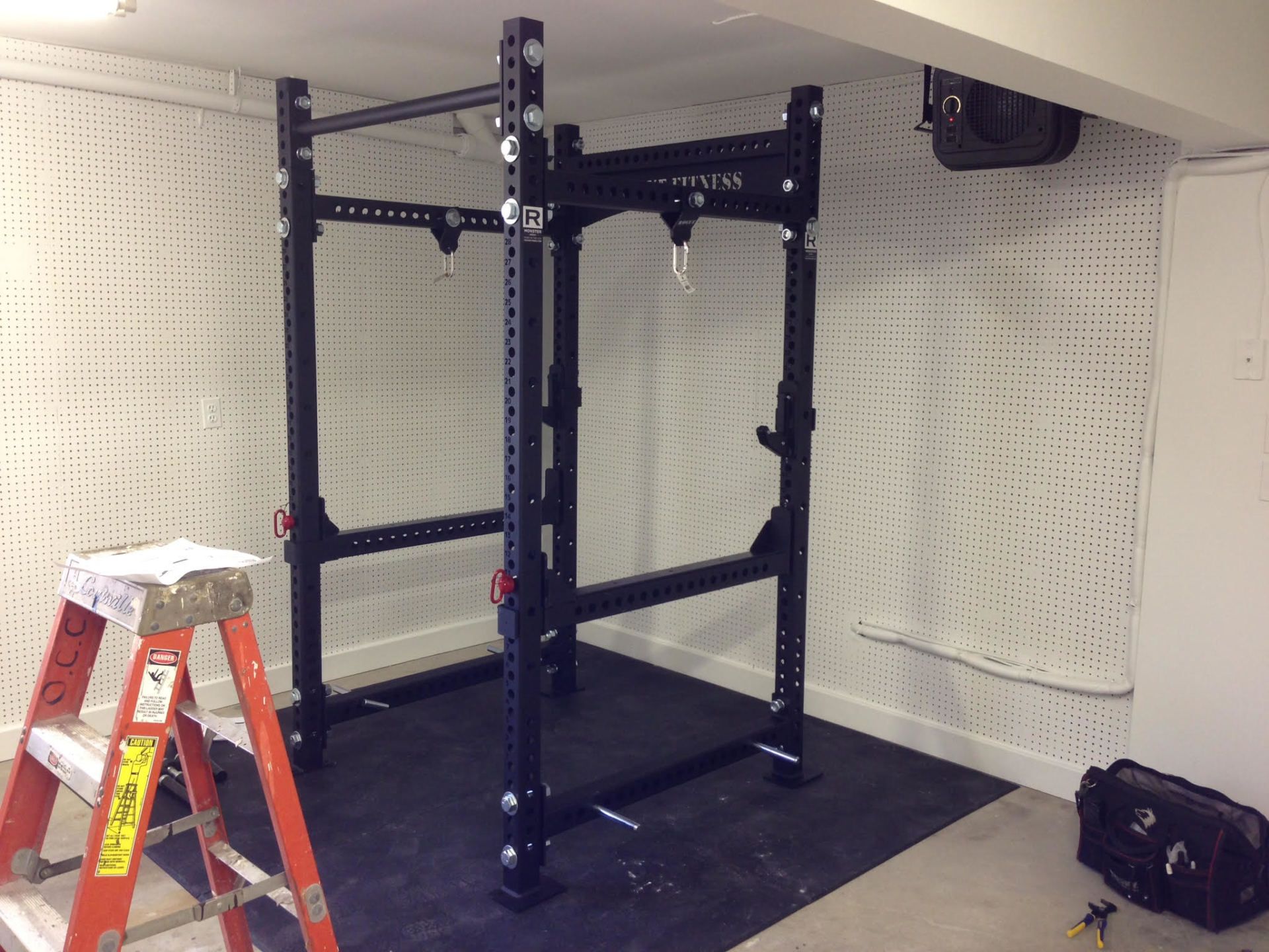 A ladder is sitting next to a squat rack in a room.