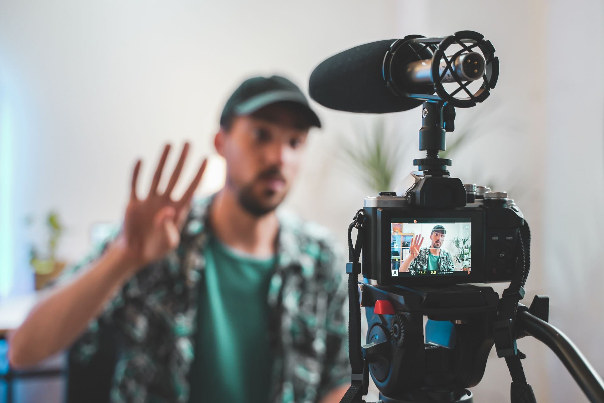 a man in a green shirt wearing a baseball cap holds 4 fingers in front of a camera he knows the difference between Film vs Video