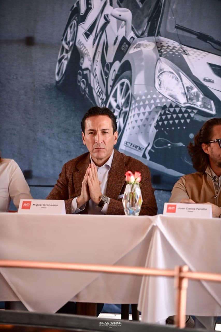Un hombre está sentado en una mesa con las manos cruzadas delante de un coche.