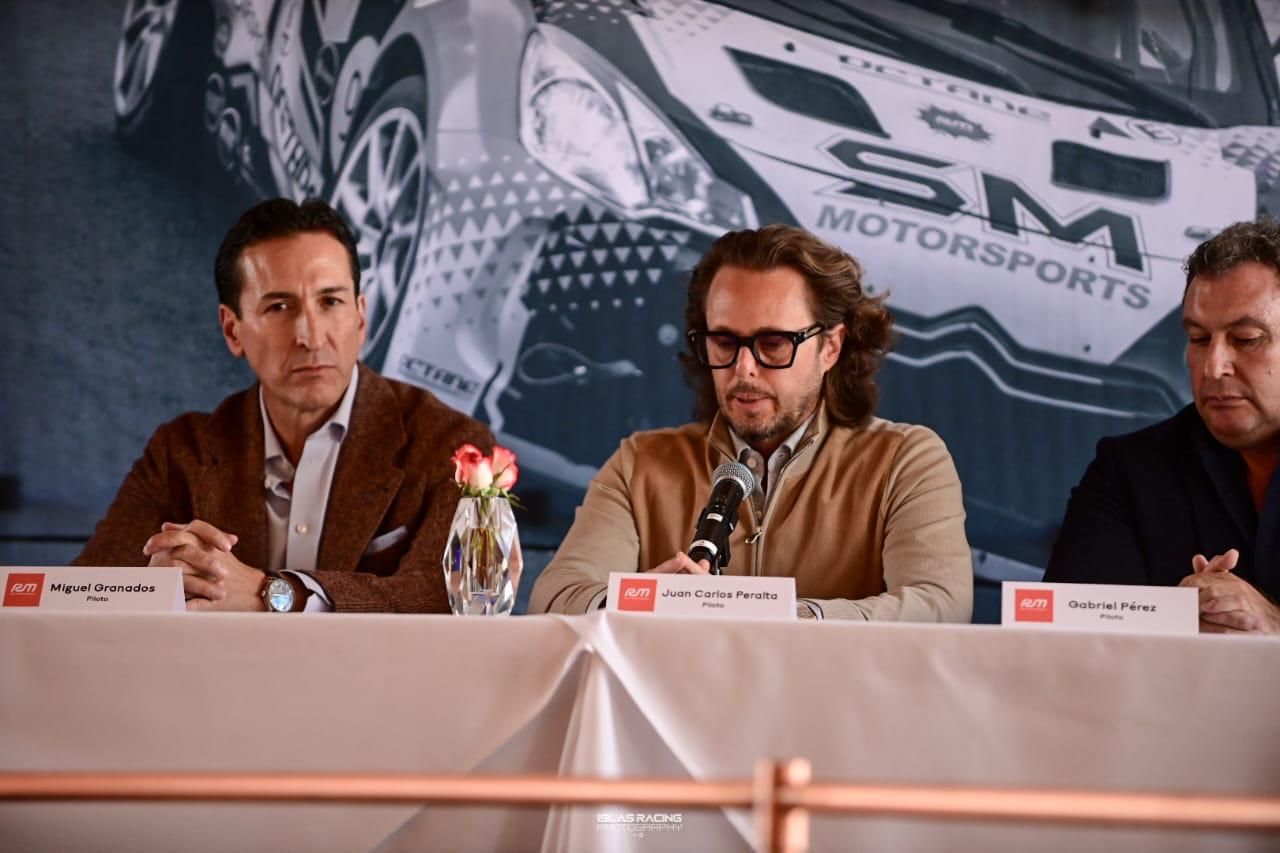 Tres hombres están sentados en una mesa frente a un cartel que dice SM Motorsports.