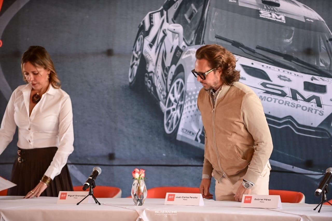 Un hombre y una mujer se sientan en una mesa frente a un automóvil deportivo SM.