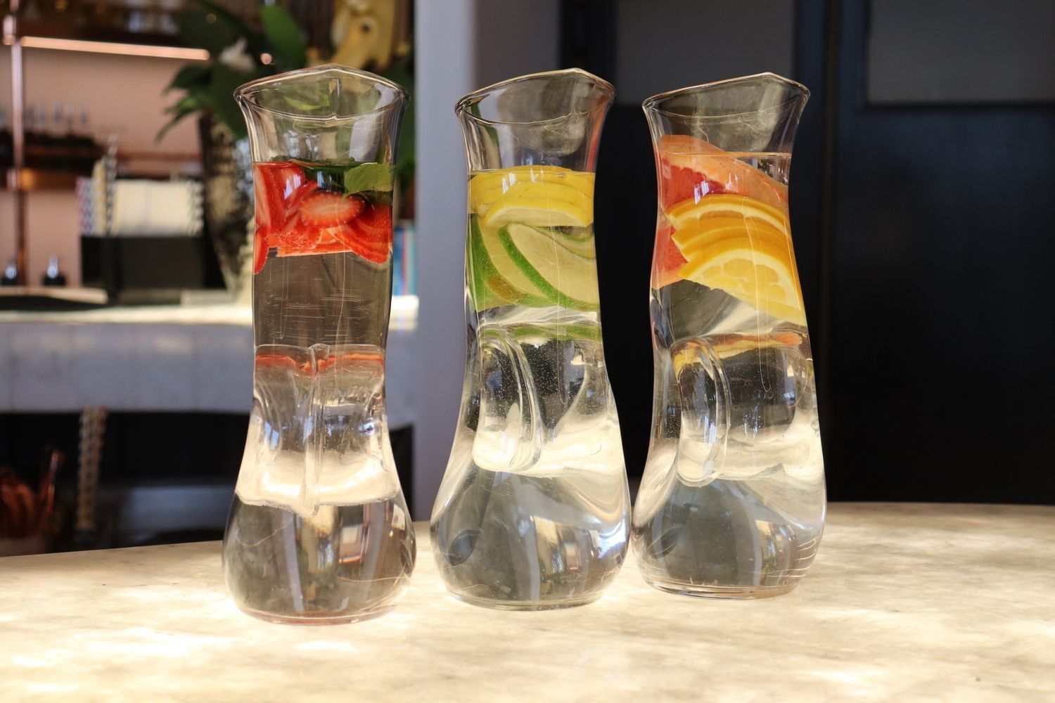 Sobre una mesa hay tres jarras llenas de agua y fruta.
