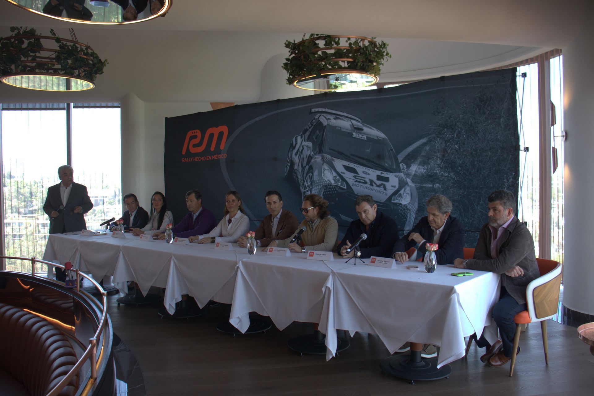 Un grupo de personas está sentado en una mesa larga frente a una pared con un automóvil encima.