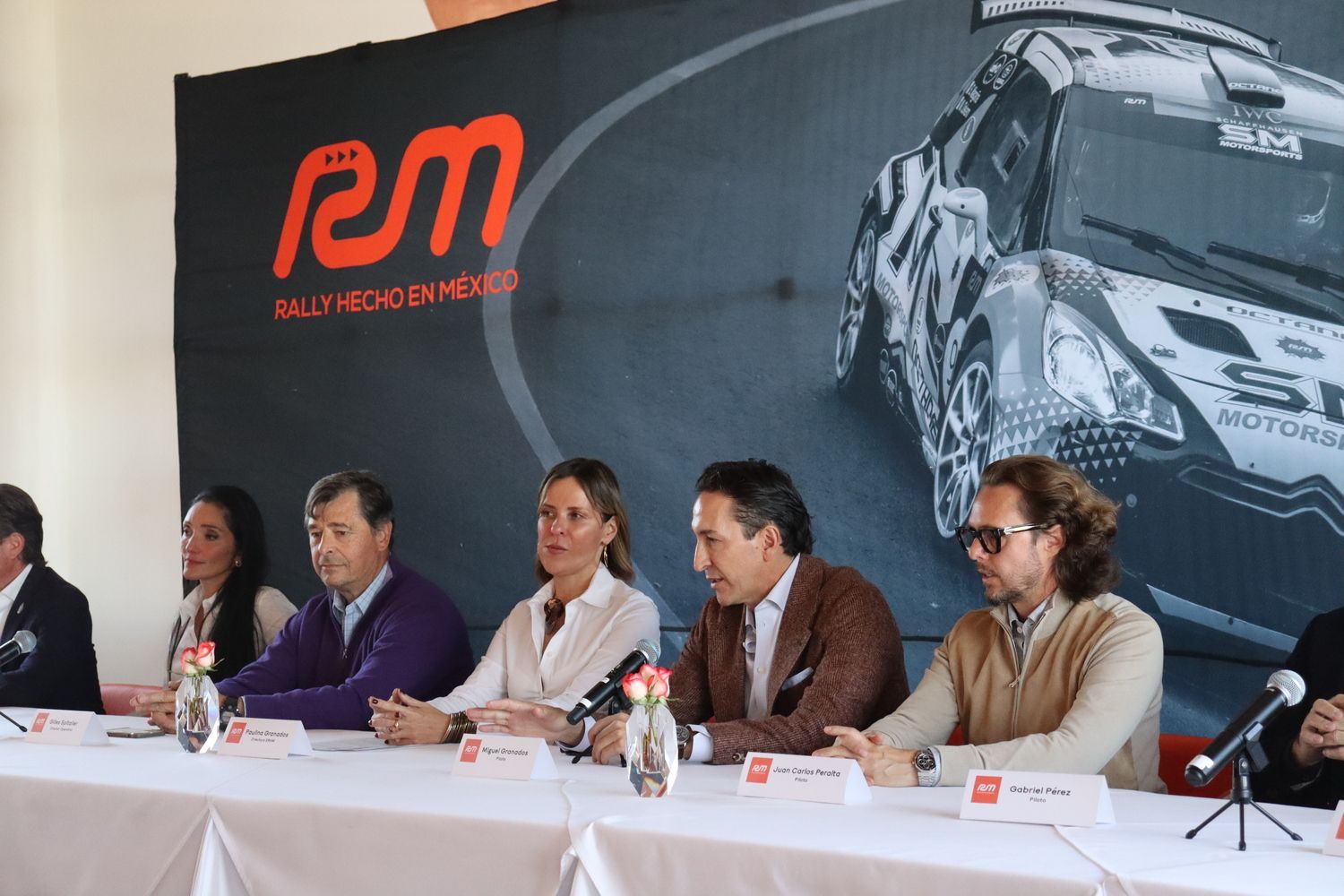 Un grupo de personas están sentadas en una mesa frente a un cartel que dice rm