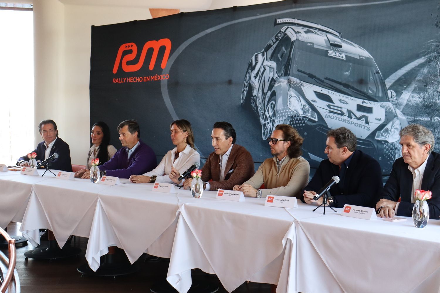 Un grupo de personas está sentado en una mesa larga con micrófonos.