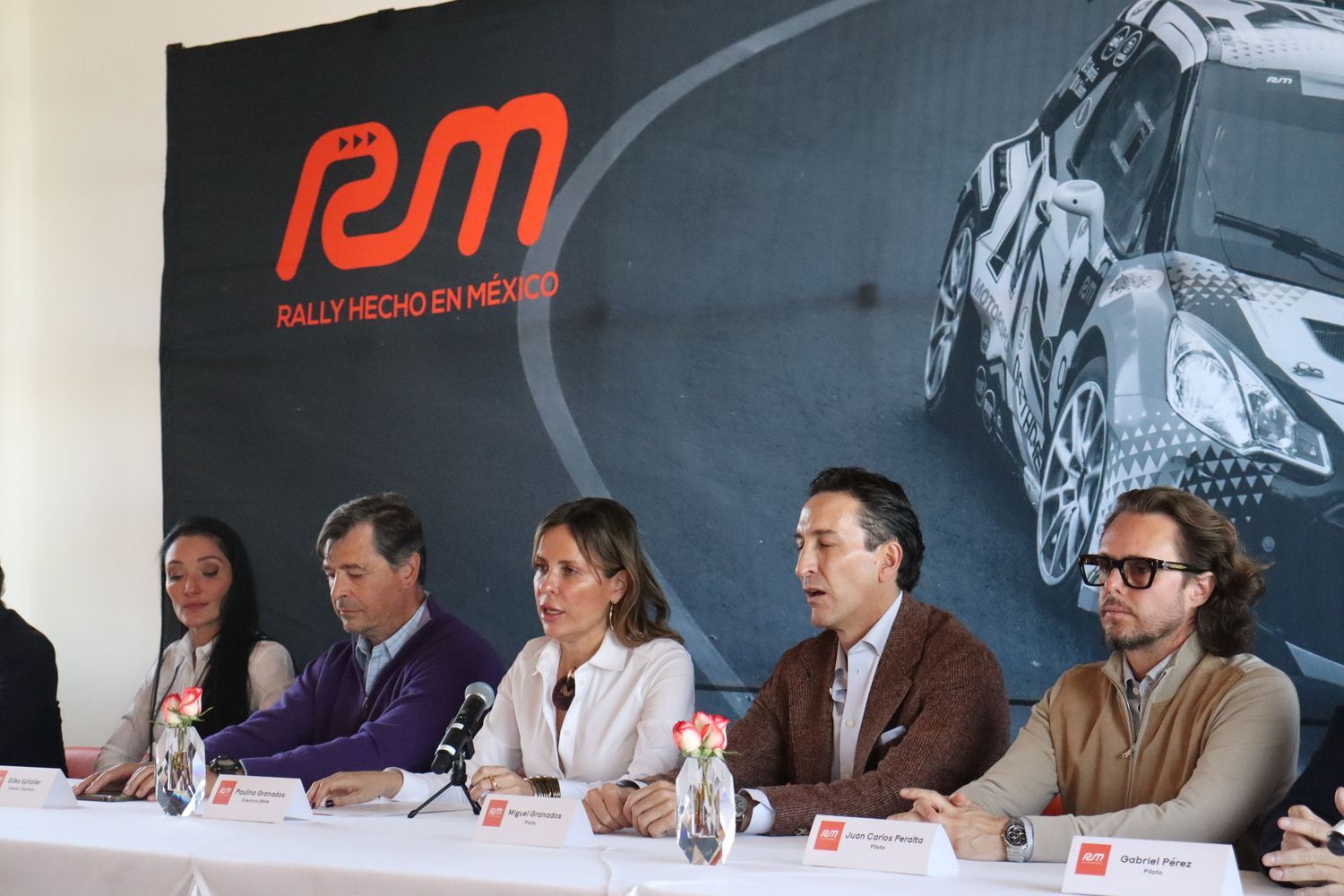 Un grupo de personas sentadas en una mesa frente a un cartel que dice rally hecho en mexico