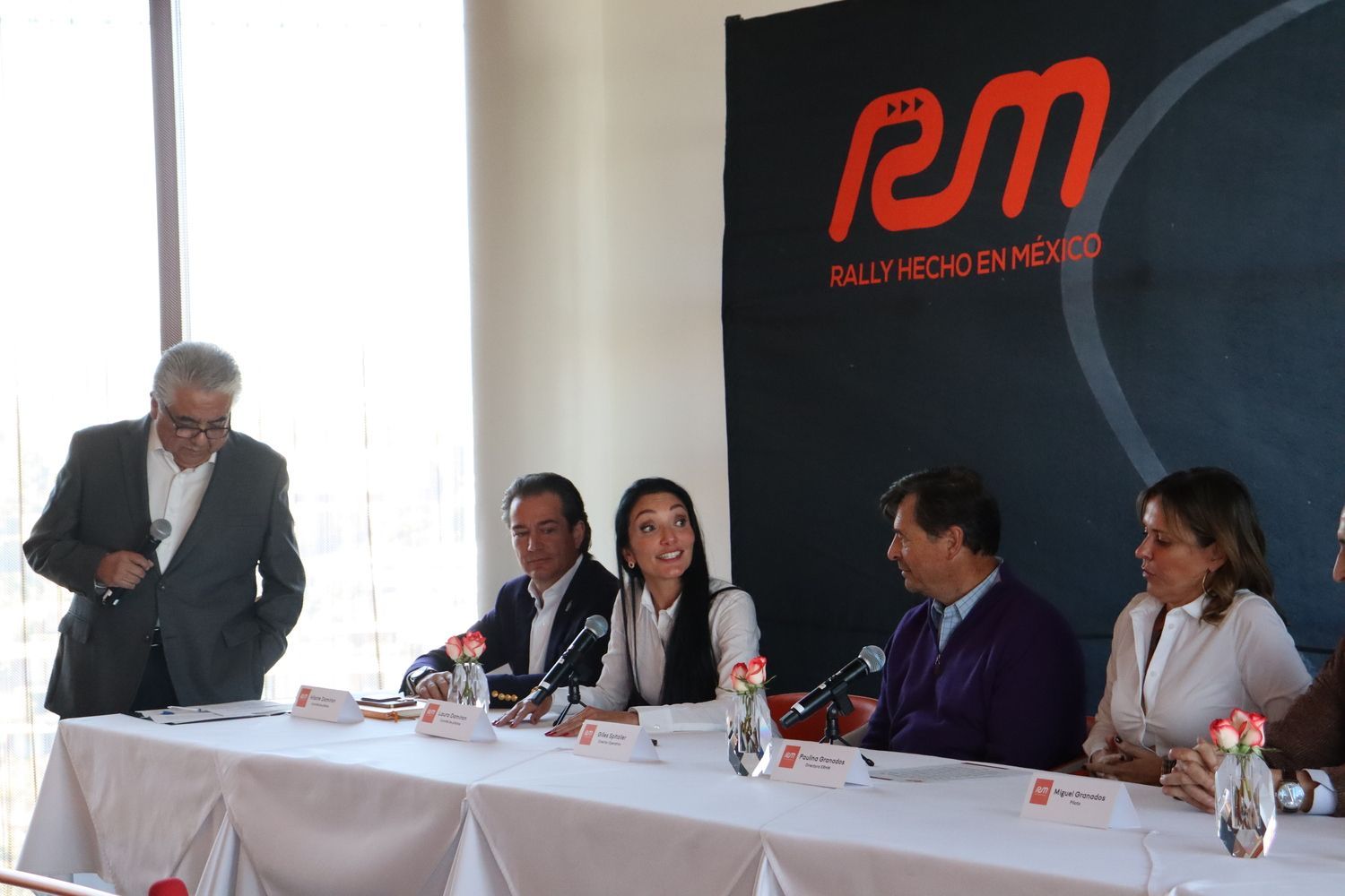 Un grupo de personas están sentadas en una mesa frente a un cartel que dice em