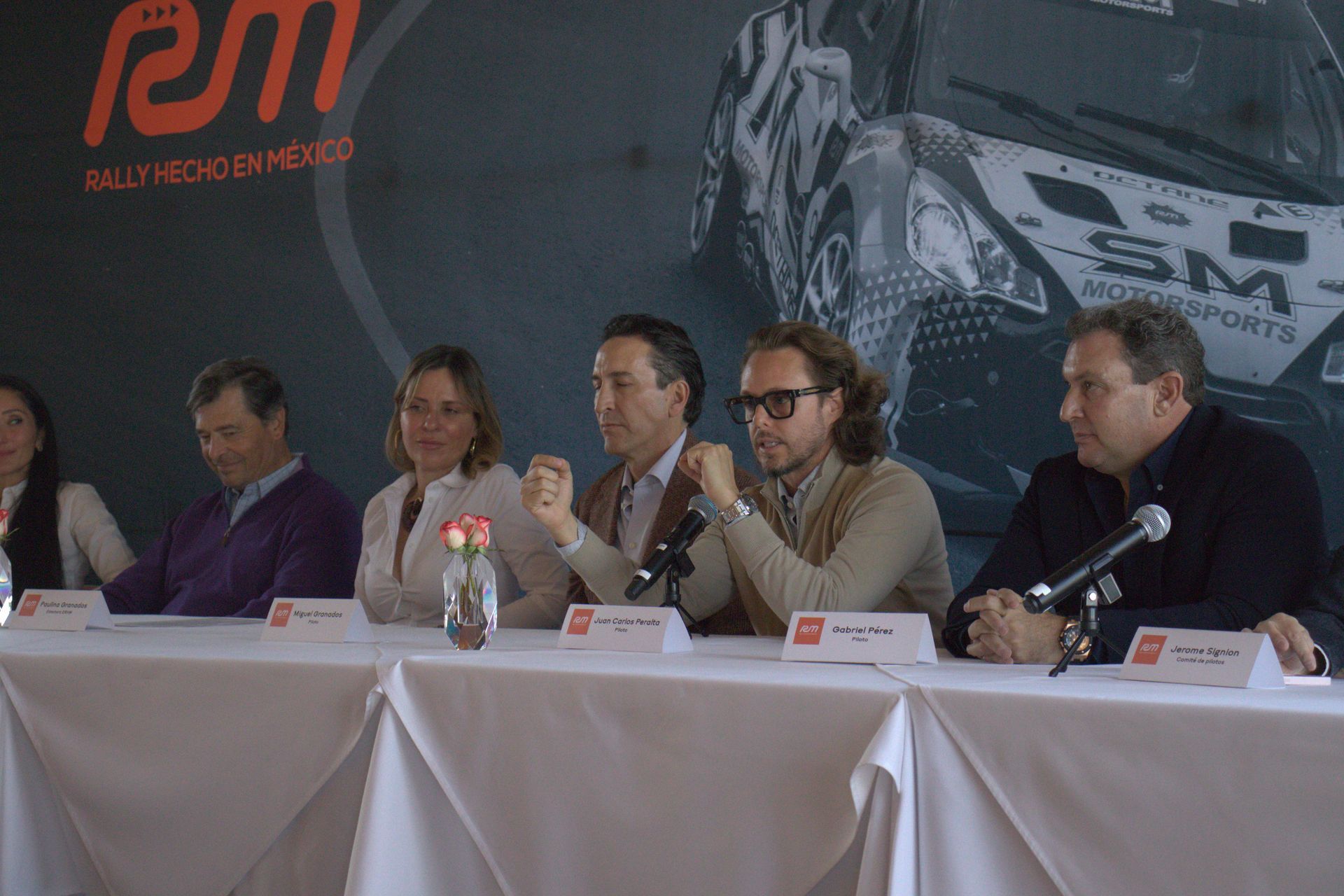 Un grupo de personas están sentadas en una mesa frente a un cartel que dice sm