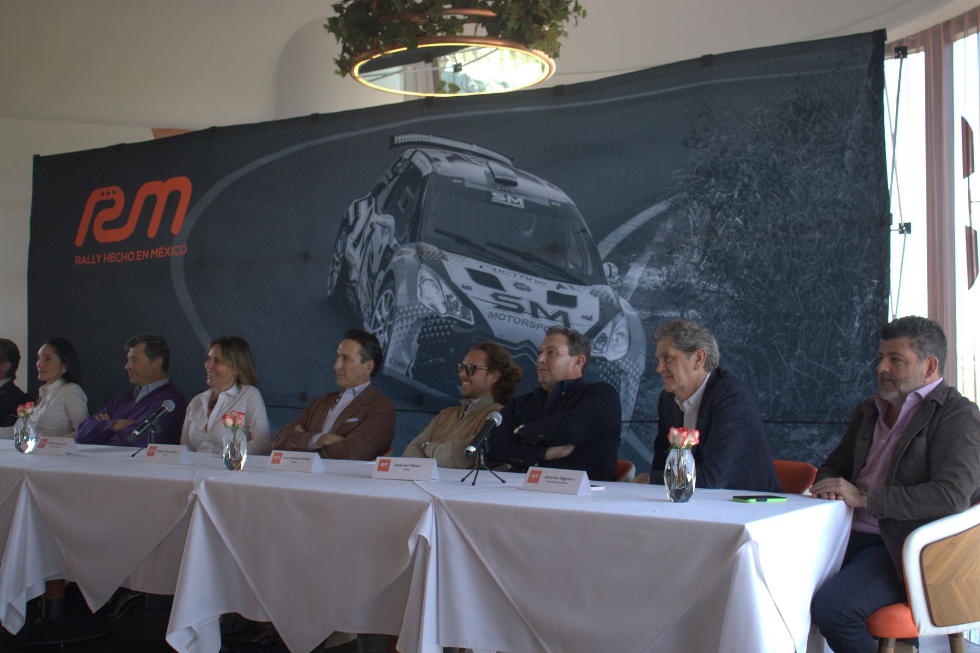Un grupo de personas se sienta en una mesa frente a una pared que dice rm