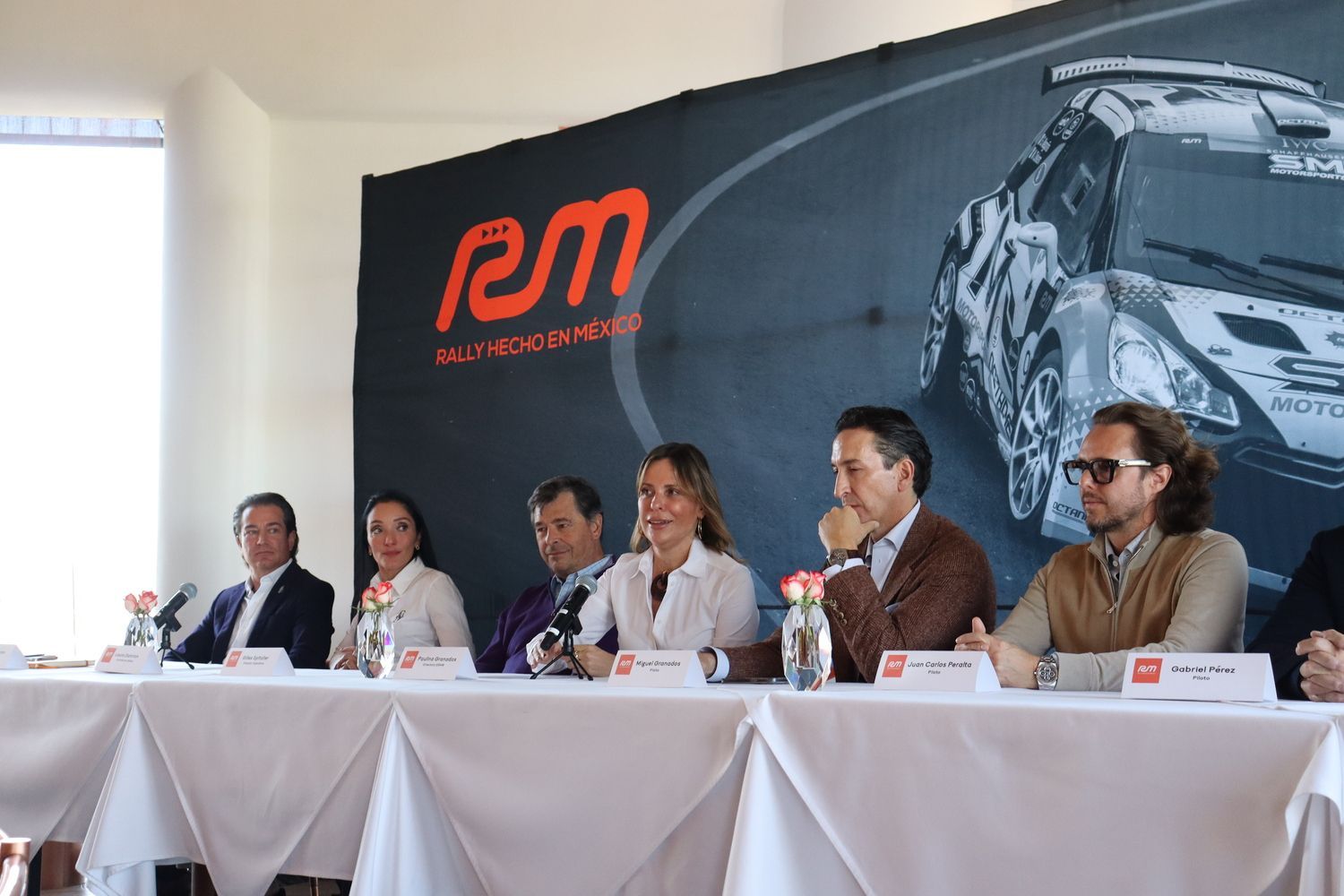 Un grupo de personas están sentadas en una mesa frente a un cartel que dice rm