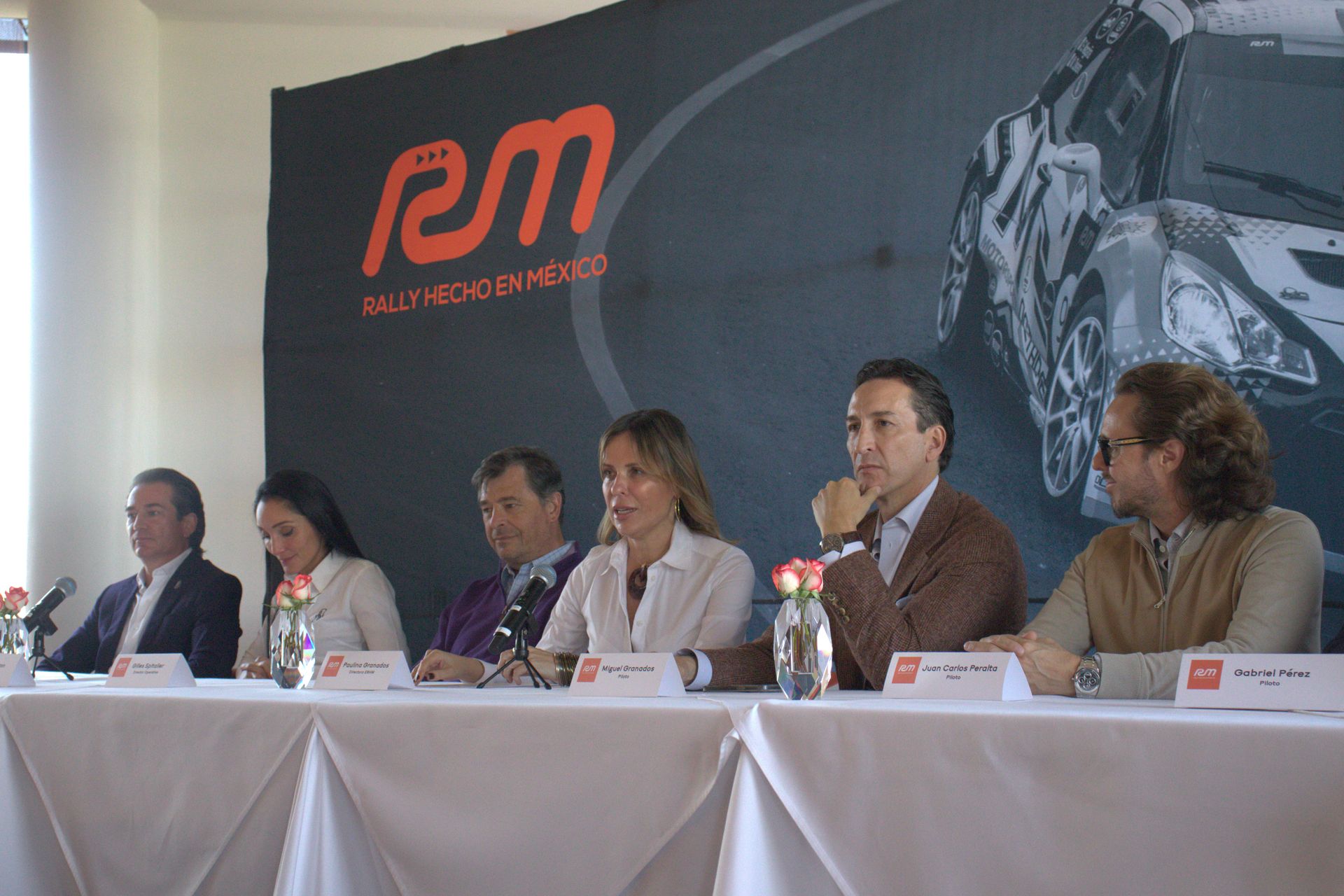 Un grupo de personas se sienta en una mesa frente a una pared que dice rm