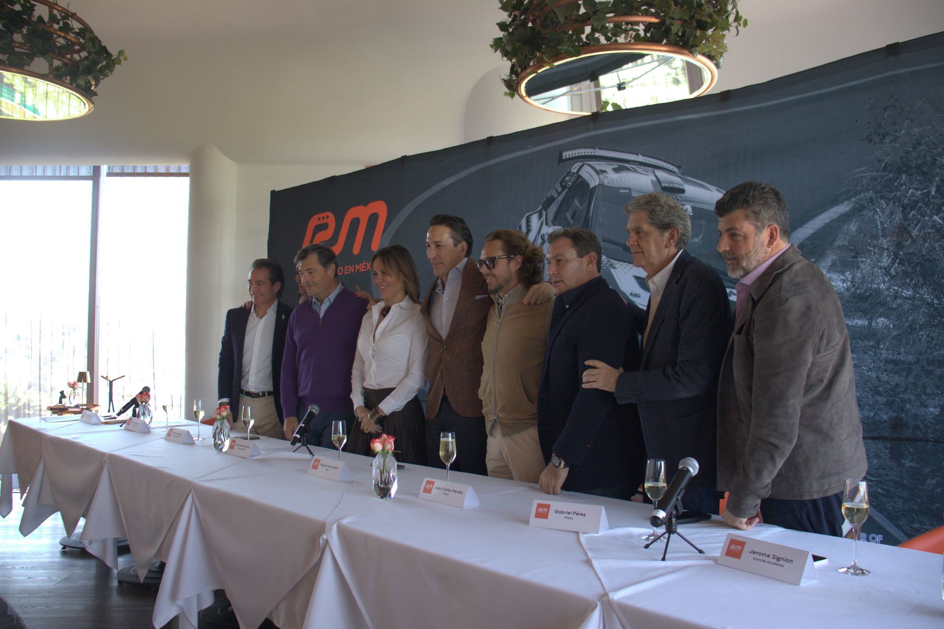 Un grupo de personas de pie alrededor de una mesa larga frente a una pared que dice pm