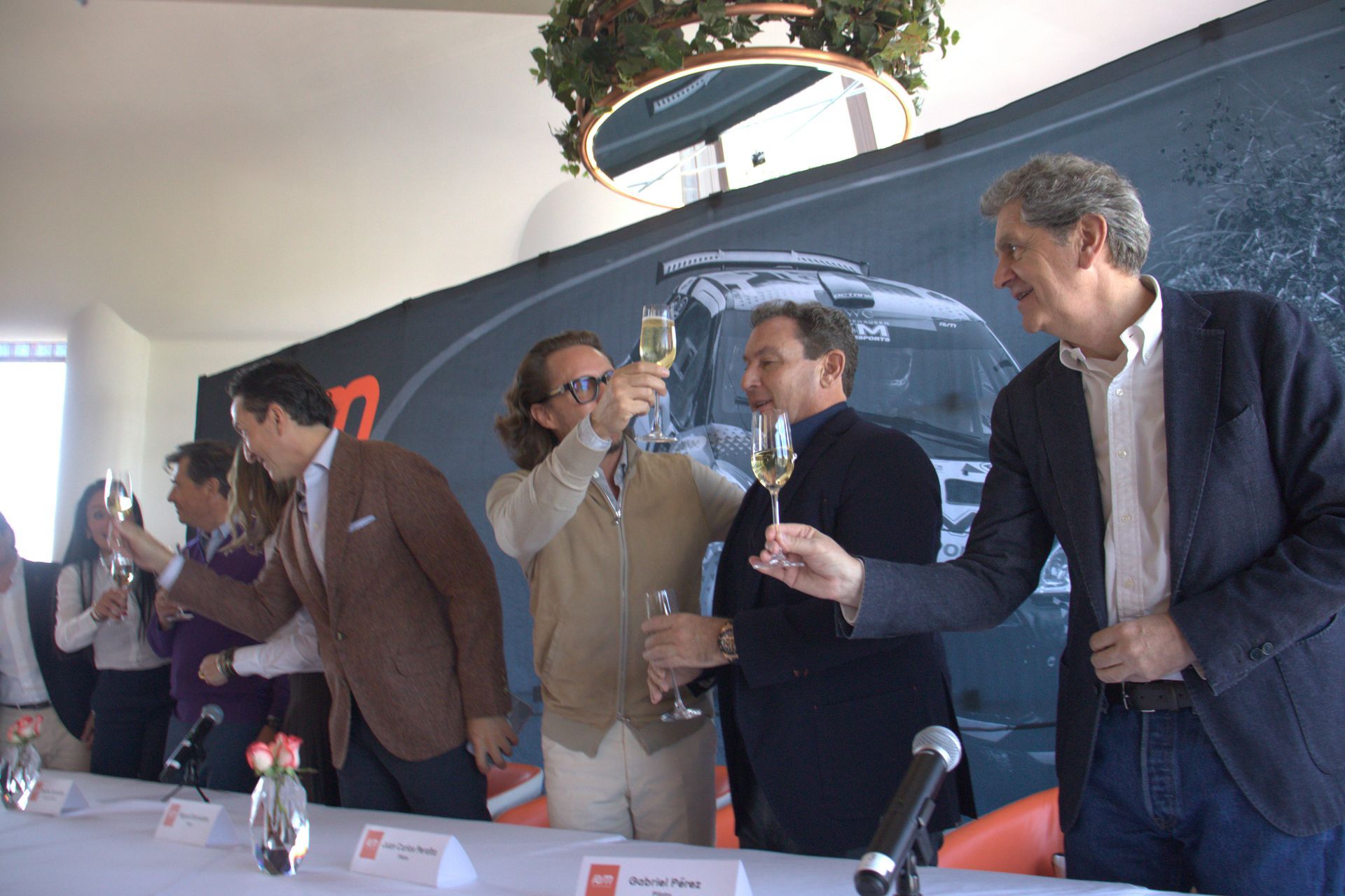 Un grupo de personas brindando con champán frente a una pared con el número 7.