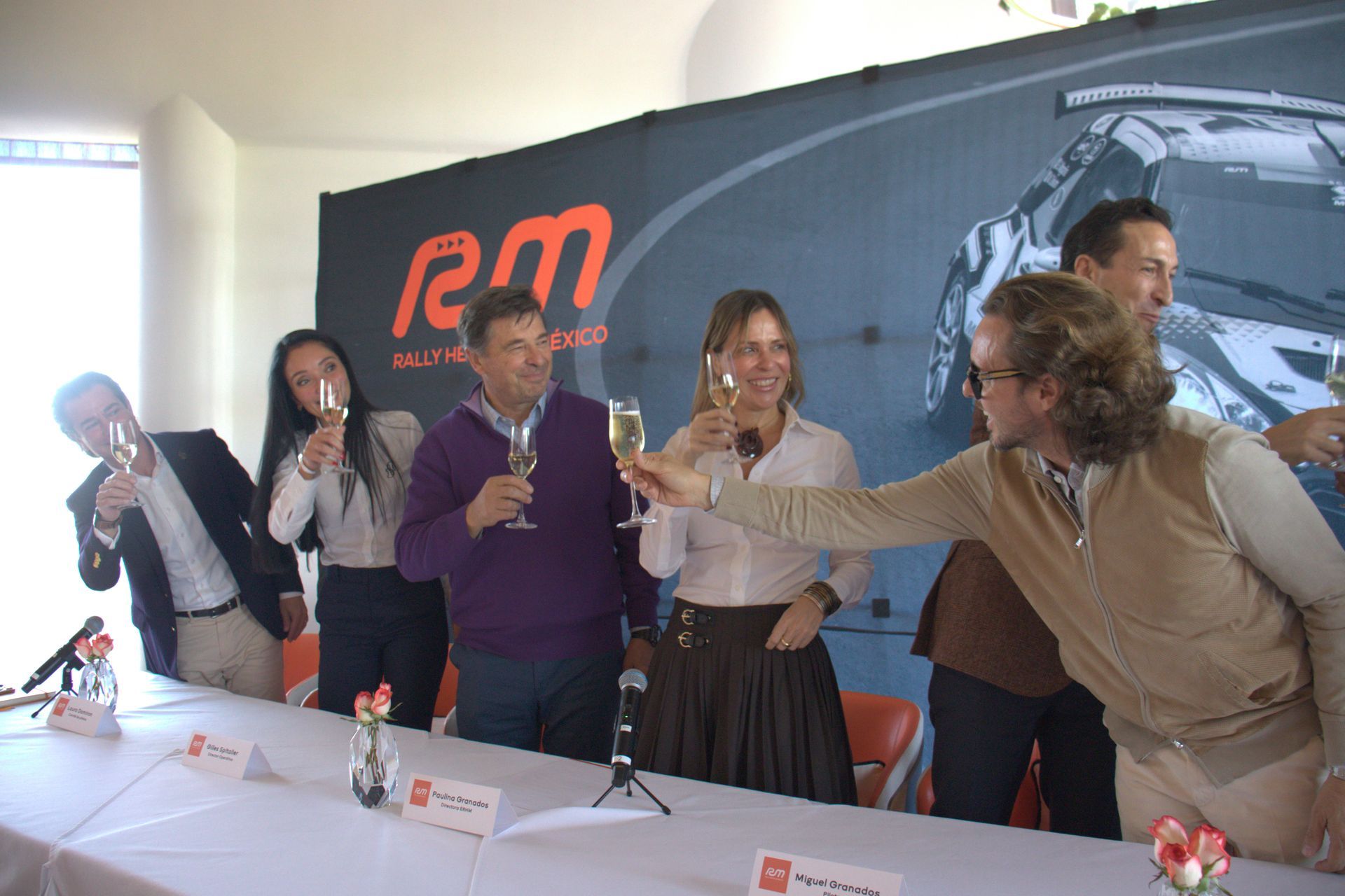 Un grupo de personas brindando con champán frente a una pared que dice RM