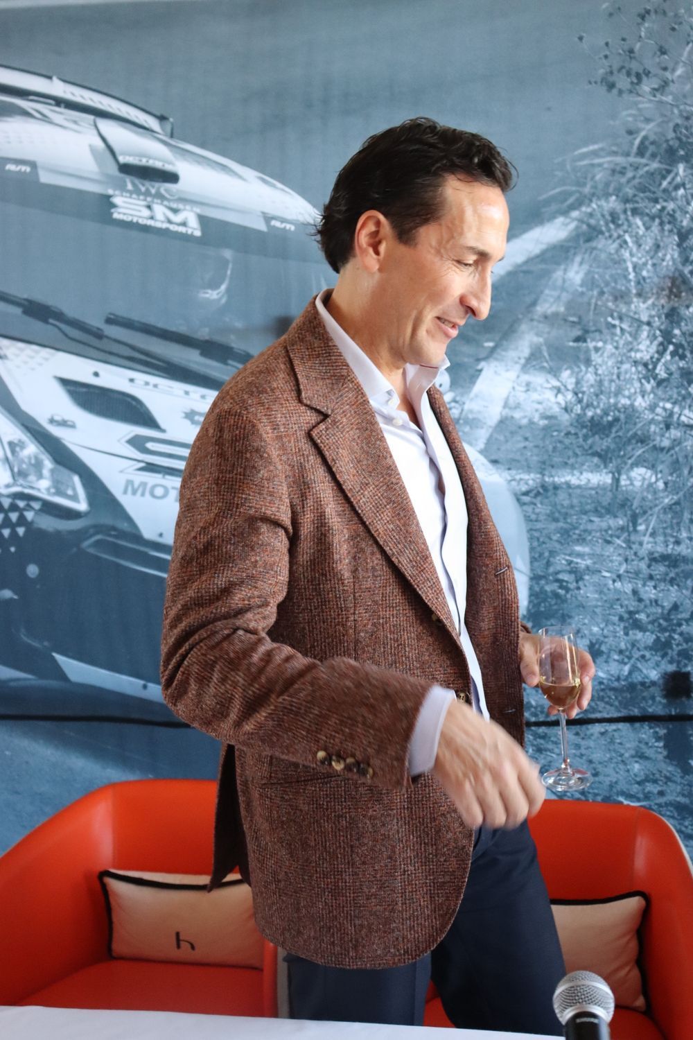 Un hombre con una chaqueta marrón sostiene una copa de vino.