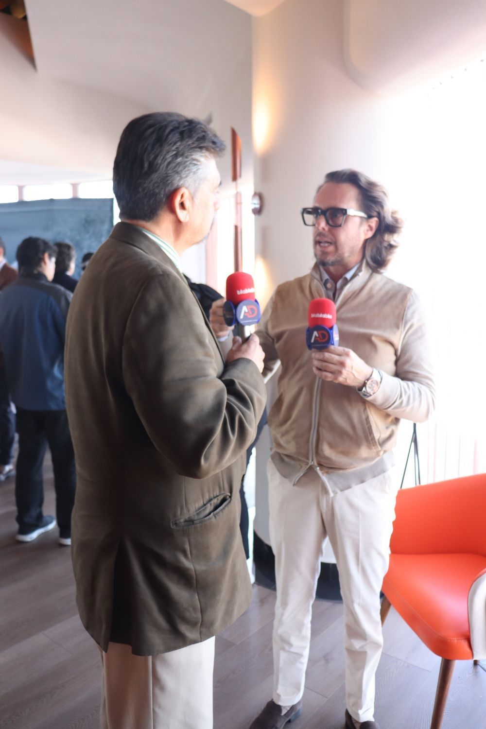 Dos hombres sostienen micrófonos y hablan entre sí.